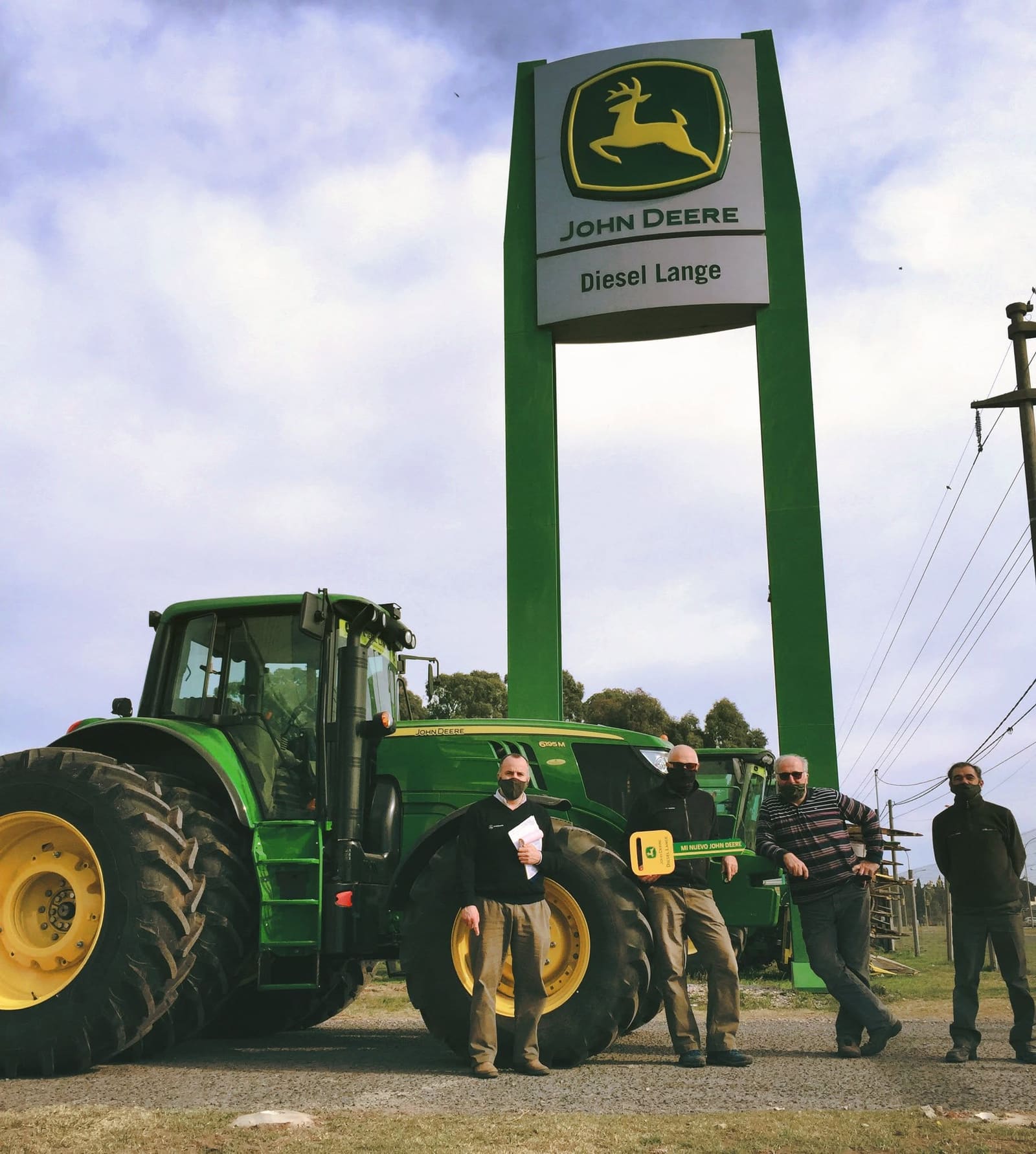 El equipo de una concesionaria John Deere frente a un tractor, bajo el cartel del local.